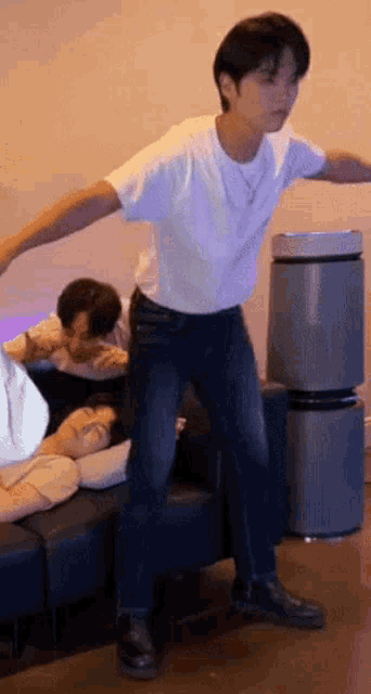 a man is standing in front of a couch with his arms outstretched while two other men sleep on it .