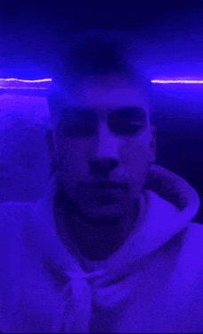 a man in a purple hoodie is standing in front of a purple light .