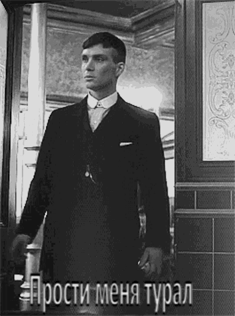 a man in a suit is standing in a doorway in a black and white photo .