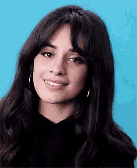 a close up of a woman 's face with a blue background . she is smiling and wearing hoop earrings .