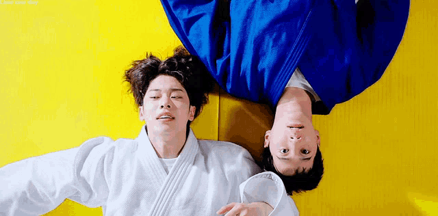 two young men are laying on their backs on a yellow mat .
