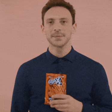 a man in a blue shirt is smiling while holding a bag of crax pretzels