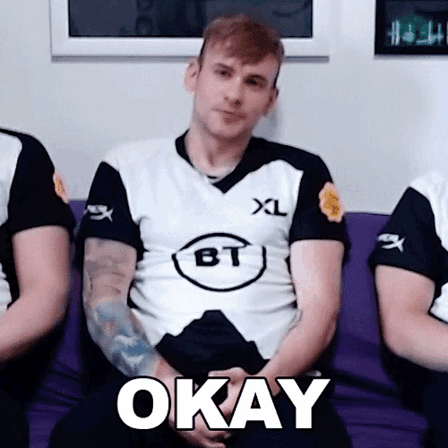 a man wearing a xl bt shirt is sitting on a couch