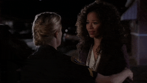 two women are hugging each other in the dark and one has a badge that says ' police ' on it