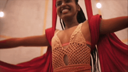 a woman in a red top is smiling while hanging in a hammock with her arms outstretched .