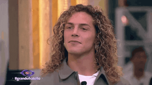 a man with long curly hair is on a television screen with the hashtag grandefratello