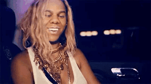 a woman wearing a white tank top and a gold necklace is smiling .