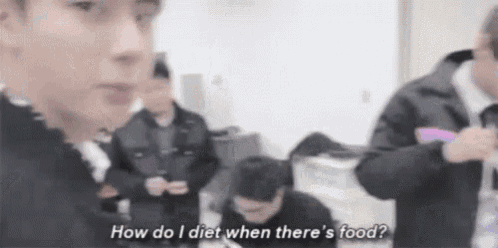 a group of people are standing around a table and one of them is asking how do i diet when there is food .