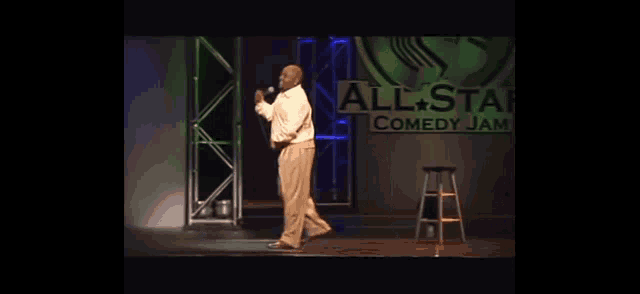 a man stands on a stage in front of a sign that says all star comedy