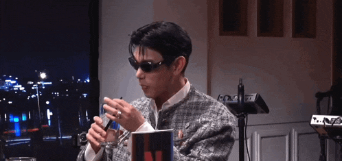 a man wearing sunglasses is sitting in a room holding a glass of water .