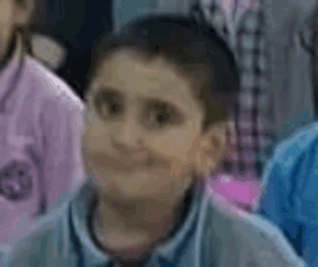 a young boy is smiling while sitting in a classroom surrounded by other children .