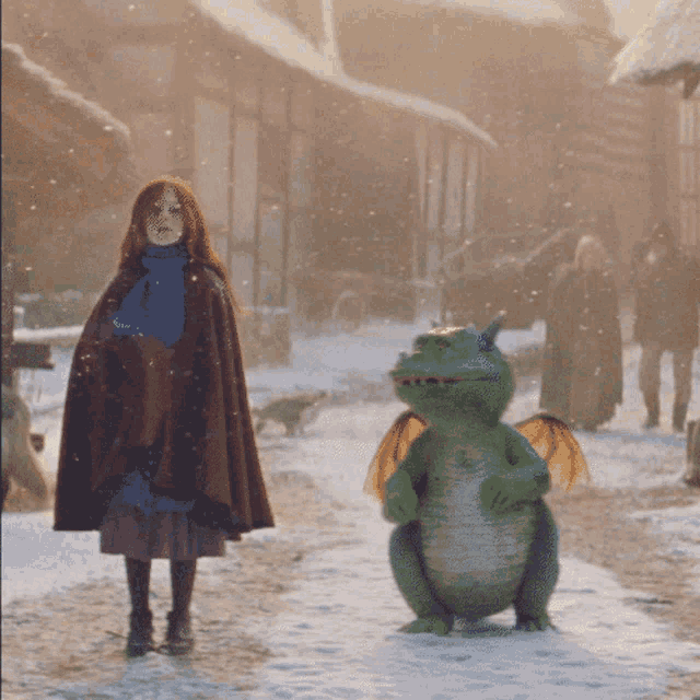 a girl in a brown cape stands next to a green dragon in the snow