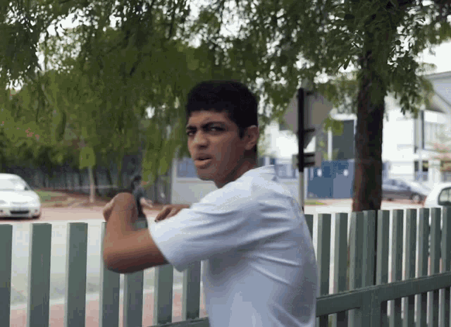 a young man in a white shirt stands behind a fence