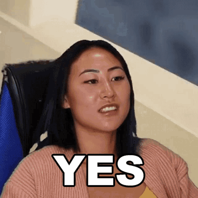 a woman in a pink sweater is sitting in a chair with the word yes written on her face .