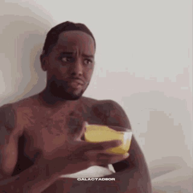 a shirtless man is holding a glass of orange juice and making a funny face .