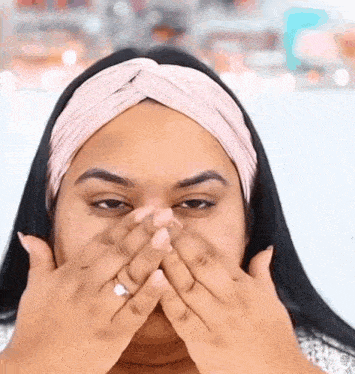 a woman wearing a headband covering her face with her hands .