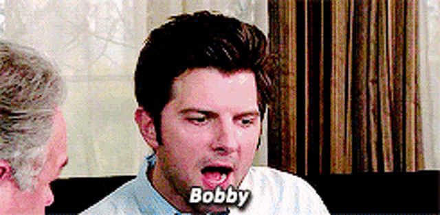 a man is sitting on a couch with his mouth open and the word bobby written on his face .