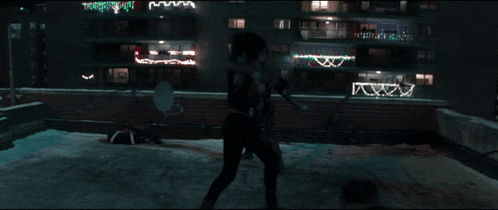 a woman is standing on a rooftop with christmas lights on the building in the background