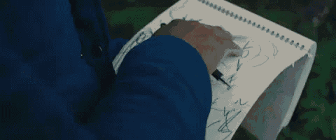 a person in a blue jacket is writing on a piece of paper with a pen .