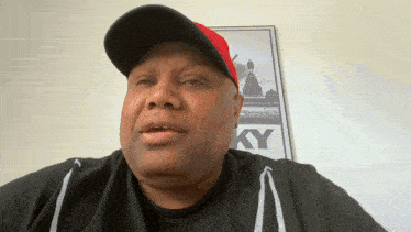 a man wearing a black shirt and a red baseball cap stands in front of a rocky poster