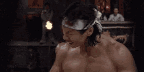 a shirtless man with a headband on his head is screaming in a boxing ring .