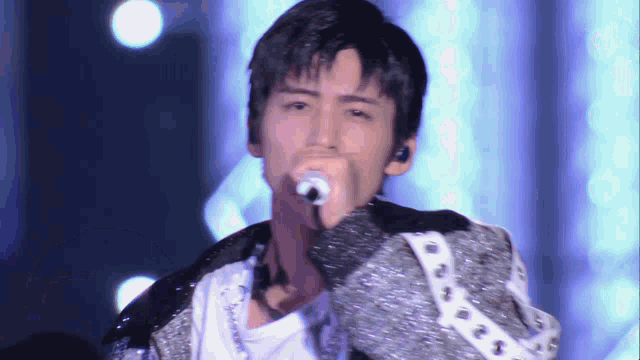 a man is singing into a microphone while wearing a jacket .