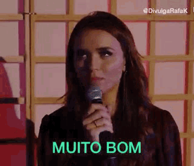 a woman is holding a microphone in her hand and says muito bom .