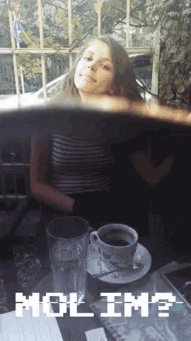 a girl sits at a table with a cup of coffee and a glass of water with mol im written on the bottom