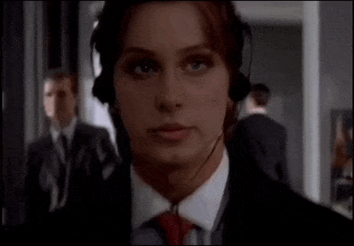 a woman wearing headphones and a tie looks at the camera