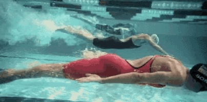 two swimmers are swimming underwater in a pool .