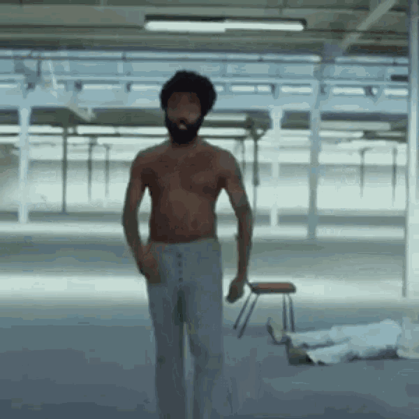 a shirtless man with a beard is standing in a room with a chair in the background .