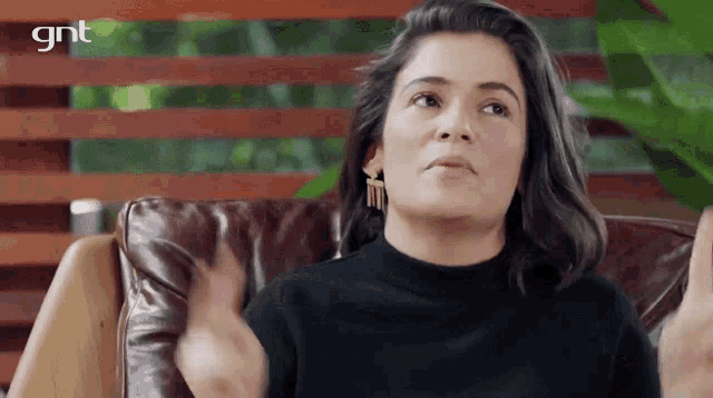 a woman in a black sweater is sitting on a leather couch with a gnt logo behind her