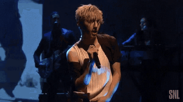 a man is singing into a microphone while a woman plays a keyboard and a man plays a guitar .