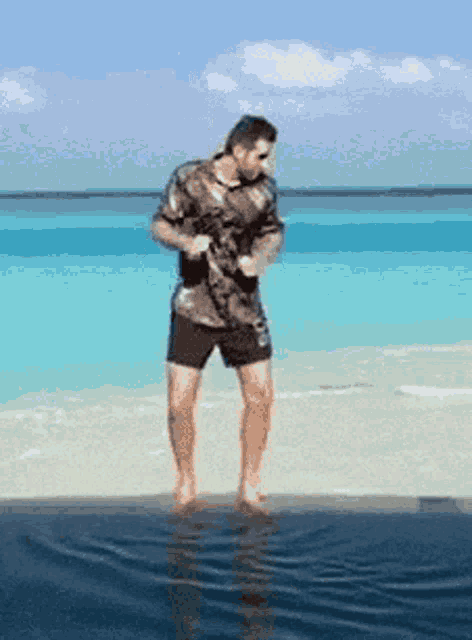 a man in a shirt and shorts is standing in the water on the beach