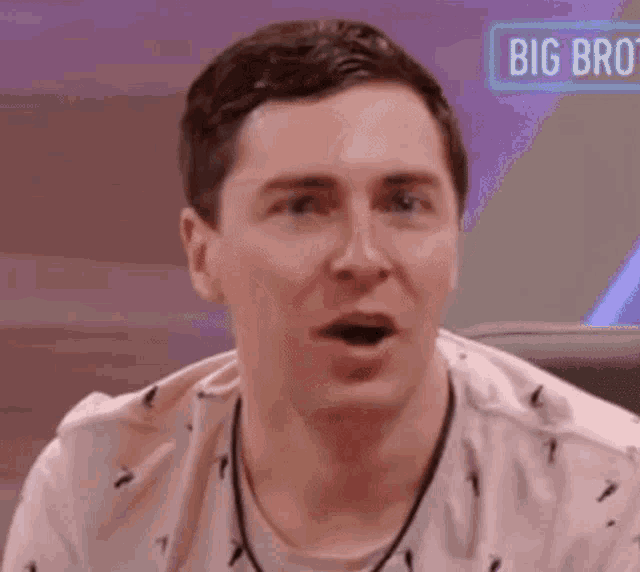 a man in a pink shirt is sitting in front of a big brother sign .