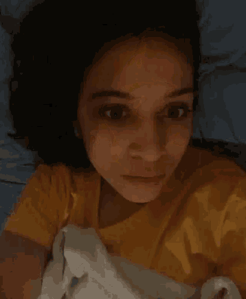 a woman in a yellow shirt is laying in bed with a white blanket