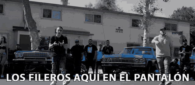 a group of people are standing in front of a building with the words los fileros aqui en el pantalon