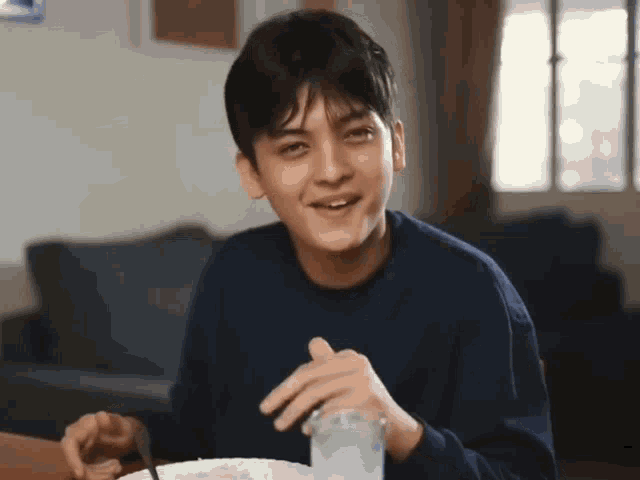 a young man sitting at a table with a plate of food and a glass