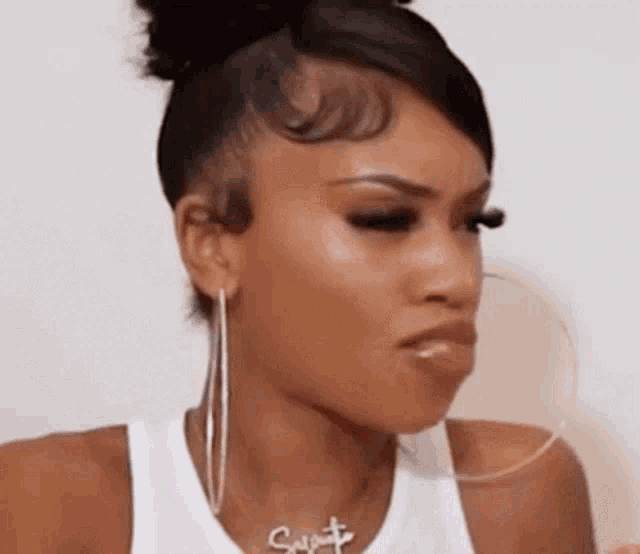 a woman wearing hoop earrings , a necklace , and a bun is making a funny face .