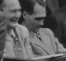 a black and white photo of a group of men sitting in a room .