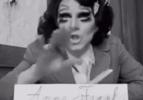 a drag queen is holding a pair of scissors and a piece of paper .