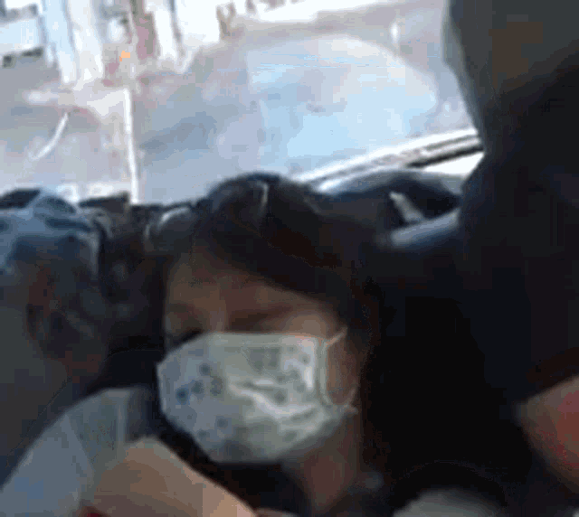 a woman wearing a face mask is sitting in a car with her eyes closed .