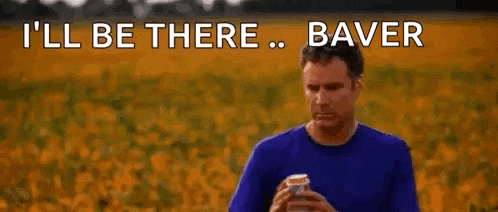 a man in a blue shirt is holding a can of beer in front of a field of flowers .