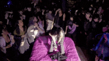 a crowd of people are gathered around a woman on a bed with a t-shirt that says " i am "