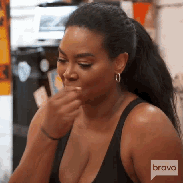 a woman is covering her mouth with her hand while wearing a black tank top and earrings .