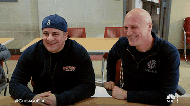 two men are sitting at a table and one has the number 3 on his cap