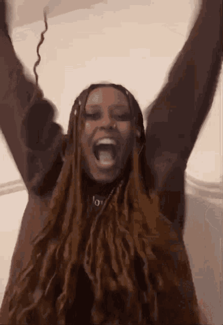 a woman with dreadlocks is holding her arms up in the air .