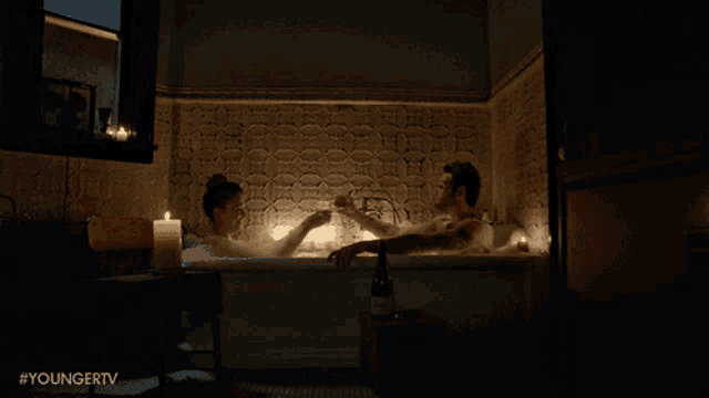 a man and a woman toasting in a bathtub with candles