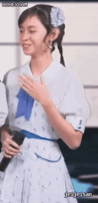 a girl in a white dress with a blue bow holds a microphone .