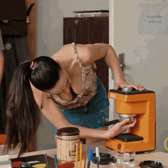 a woman is using an orange coffee maker with a sign on the wall that says ponavodna